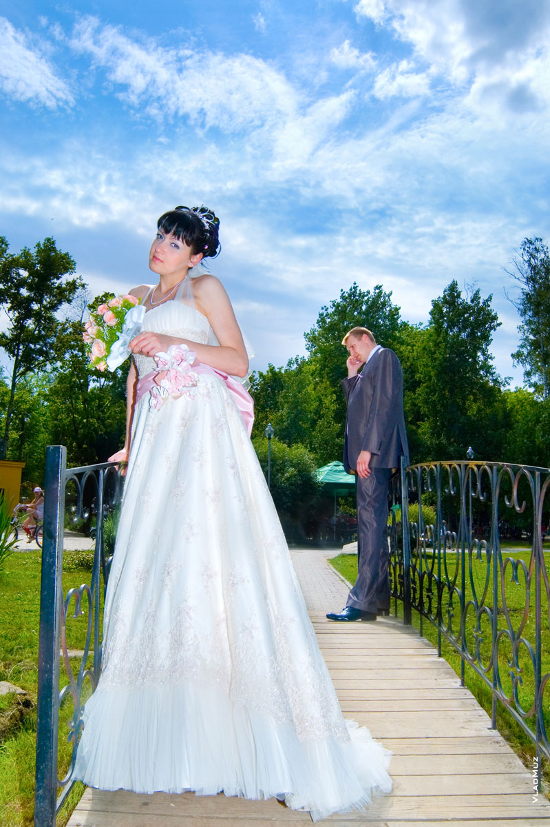 Фото на мостике в Центральном парке культуры и отдыха Мытищ: невеста впереди, вдали стоит жених