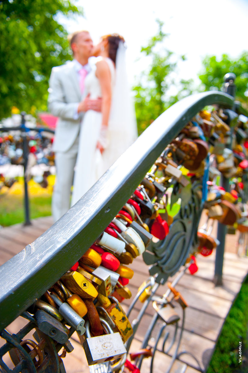 Фото поцелуя новобрачных на мостике влюбленных в Королёве на фоне свадебных замочков