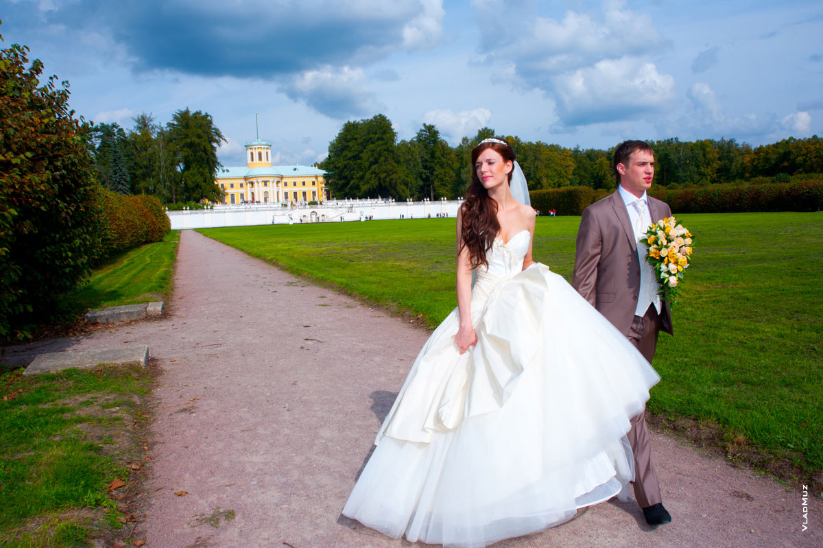 Фото идущих жениха с невестой по краю Большого партера на фоне фасада дворца и террас в Архангельском