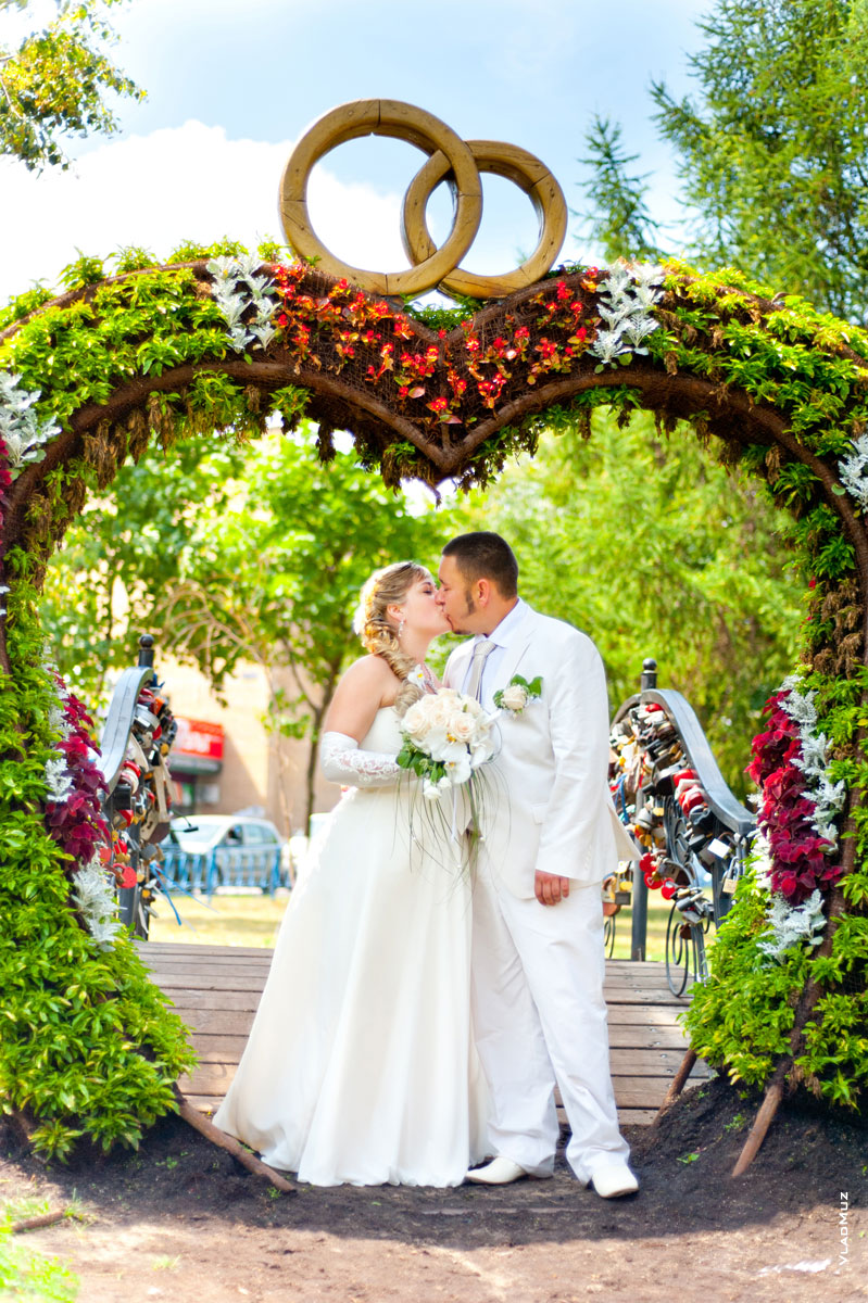 Фото молодоженов в свадебной сердечной арке с кольцами вверху на проспекте Королева