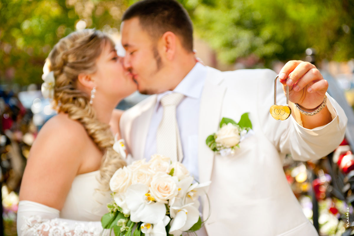 Свадебное фото: свадебный замочек в фокусе, жених с невестой и их свадебный поцелуй — в расфокусе
