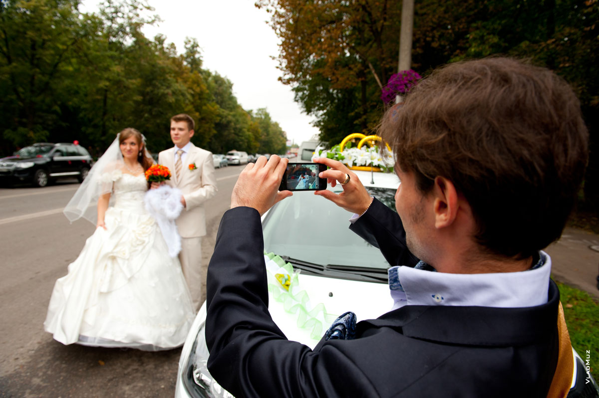 Фото свидетеля, фотографирующего подъехавших к ЗАГСу жениха с невестой