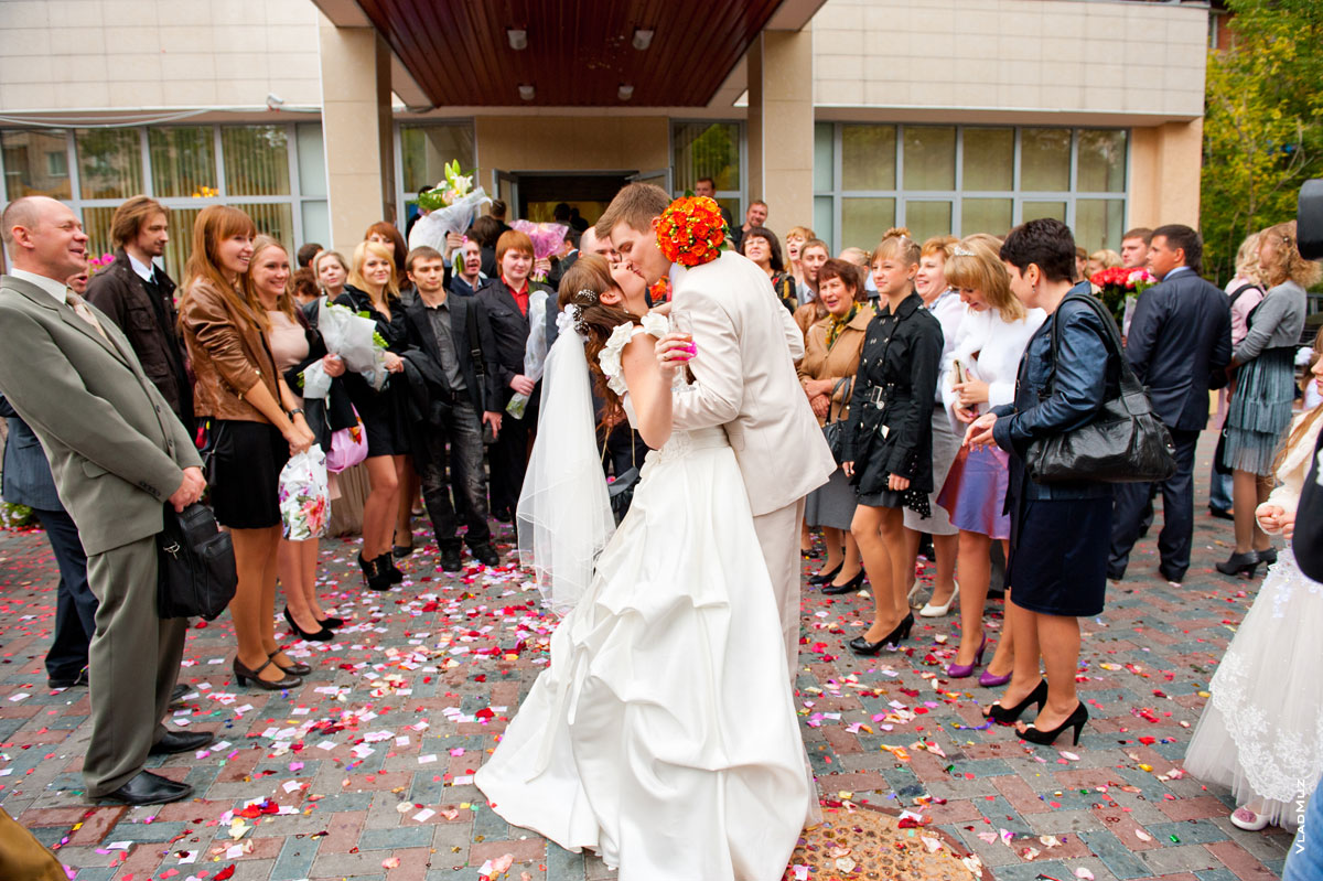 Фото крепкого свадебного поцелуя в окружении гостей перед входом в Измайловский ЗАГС Москвы