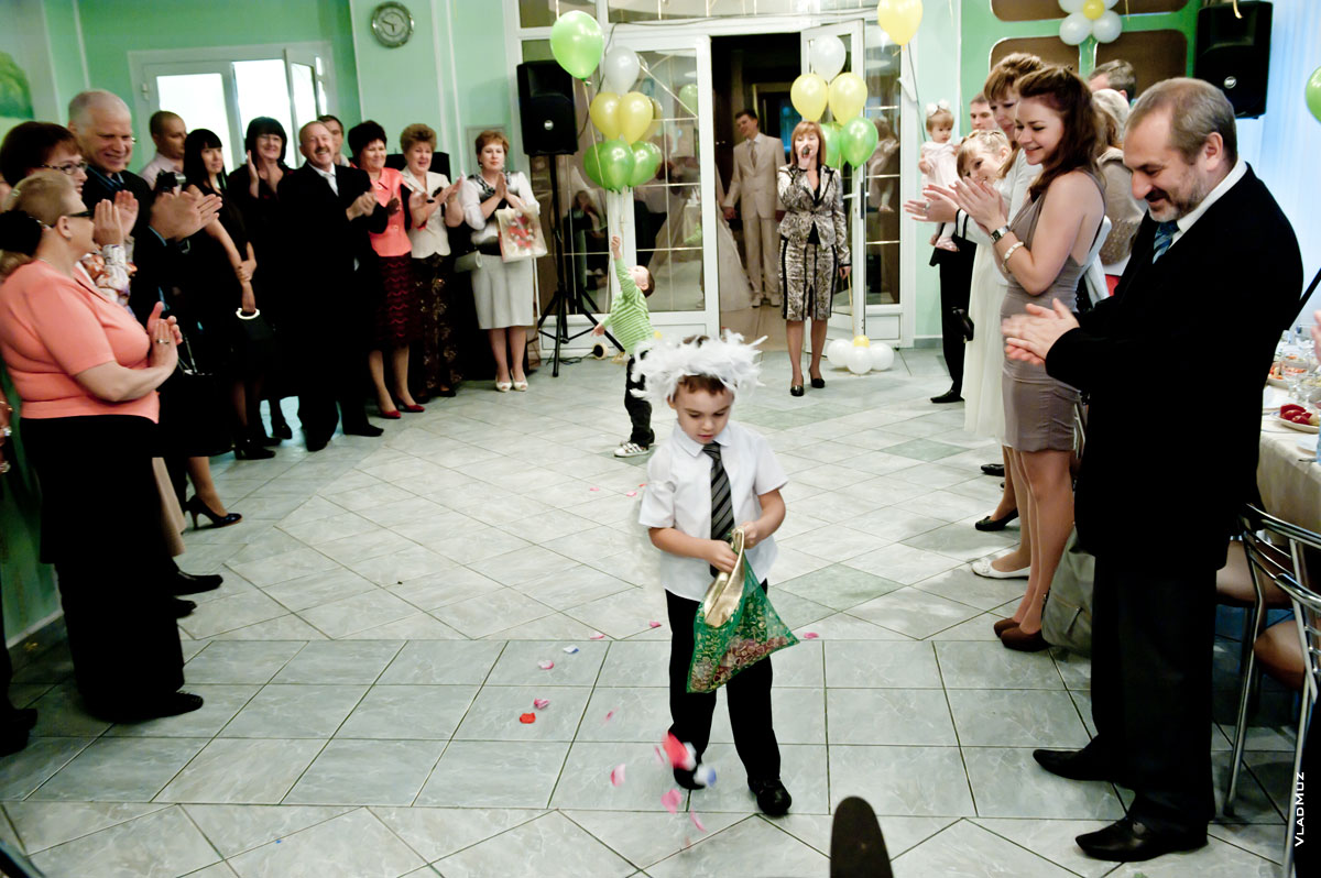 Мальчик-ангел разбрасывает лепестки роз и конфетти в ресторане перед входом молодоженов