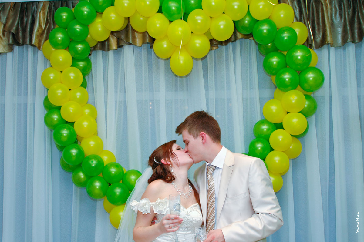 Жених и невеста целуются в ресторане на фоне сердца из воздушных шаров