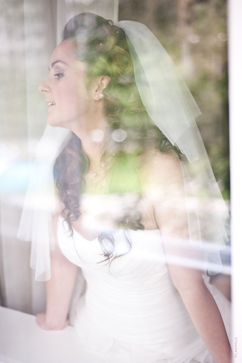 Фотопортрет невесты, выглядывающей в окно, сквозь стекло