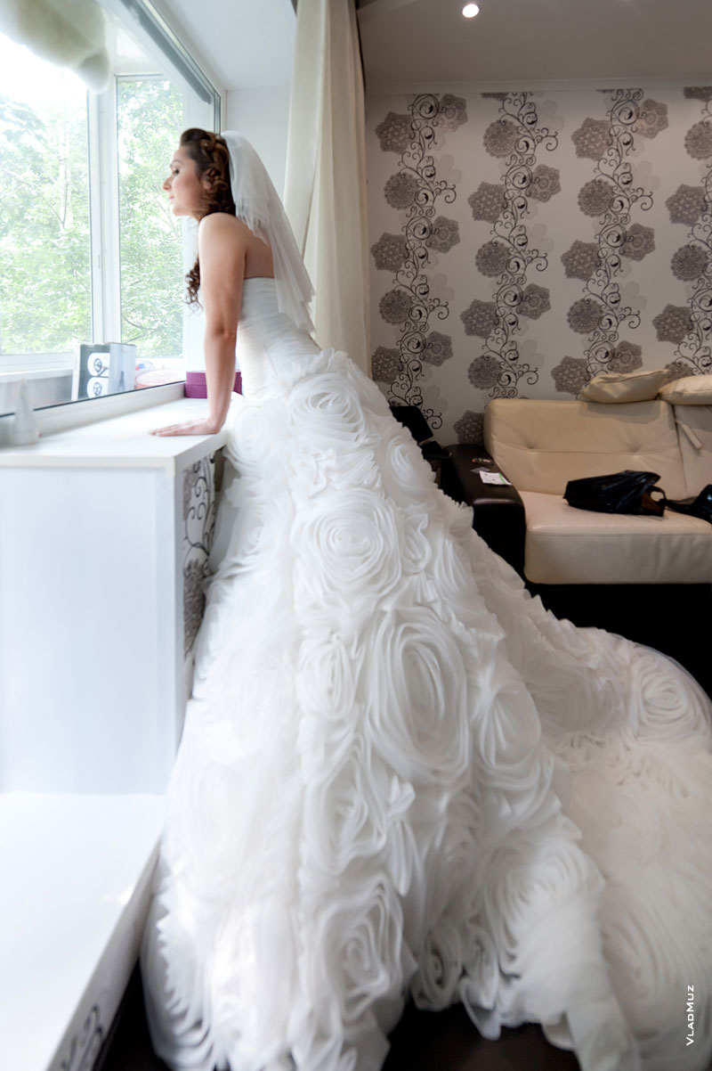 Фото невесты в свадебном платье у окна в полный рост