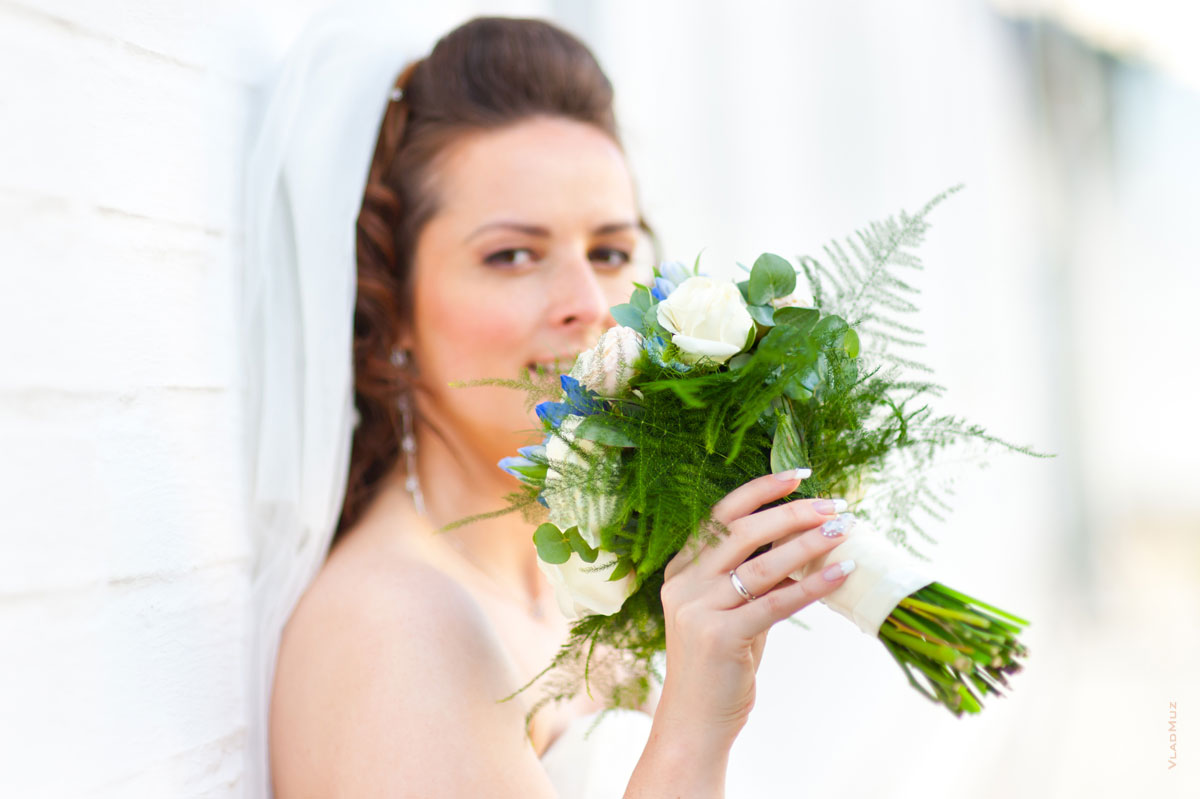 Фотопортрет невесты с букетом и обручальным кольцом на пальце в фокусе, лицо невесты в расфокусе