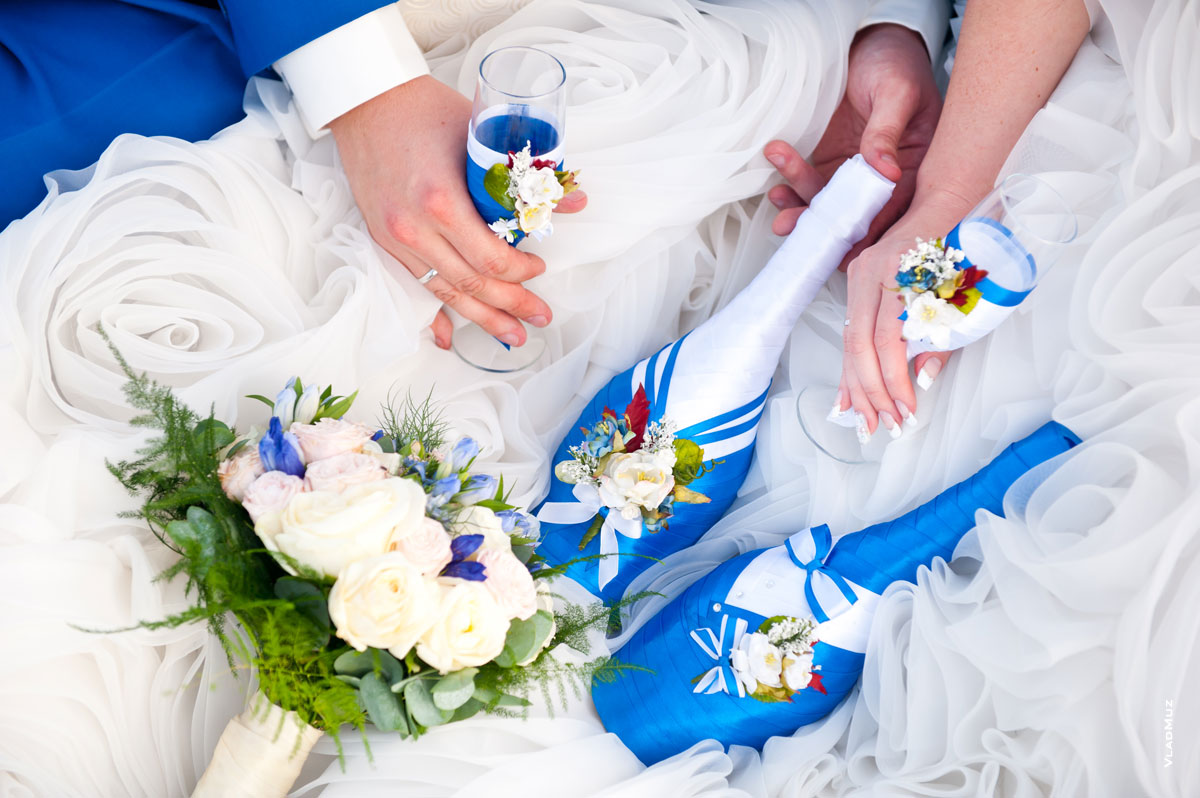 Свадебный натюрморт: букет невесты, свадебные быки и бокалы в руках жениха и невесты