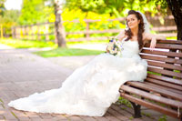 Фото невесты с букетом, сидящей на скамье, и длинный шлейф свадебного платья