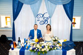 Жених и невеста за столом в Голубом зале ресторана, над ними инициалы Д и В, т.е. Дмитрий и Виктория