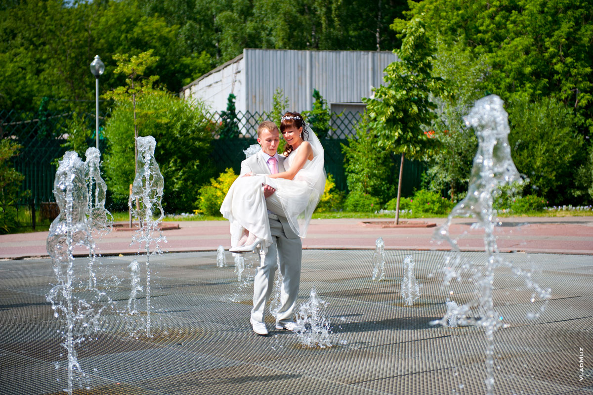 Жених ходит с невестой на руках над танцующим, музыкальным фонтаном в парке Мытищ
