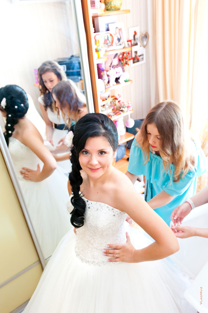 Фото невесты и подружек, затягивающих невесте корсет на свадебном платье