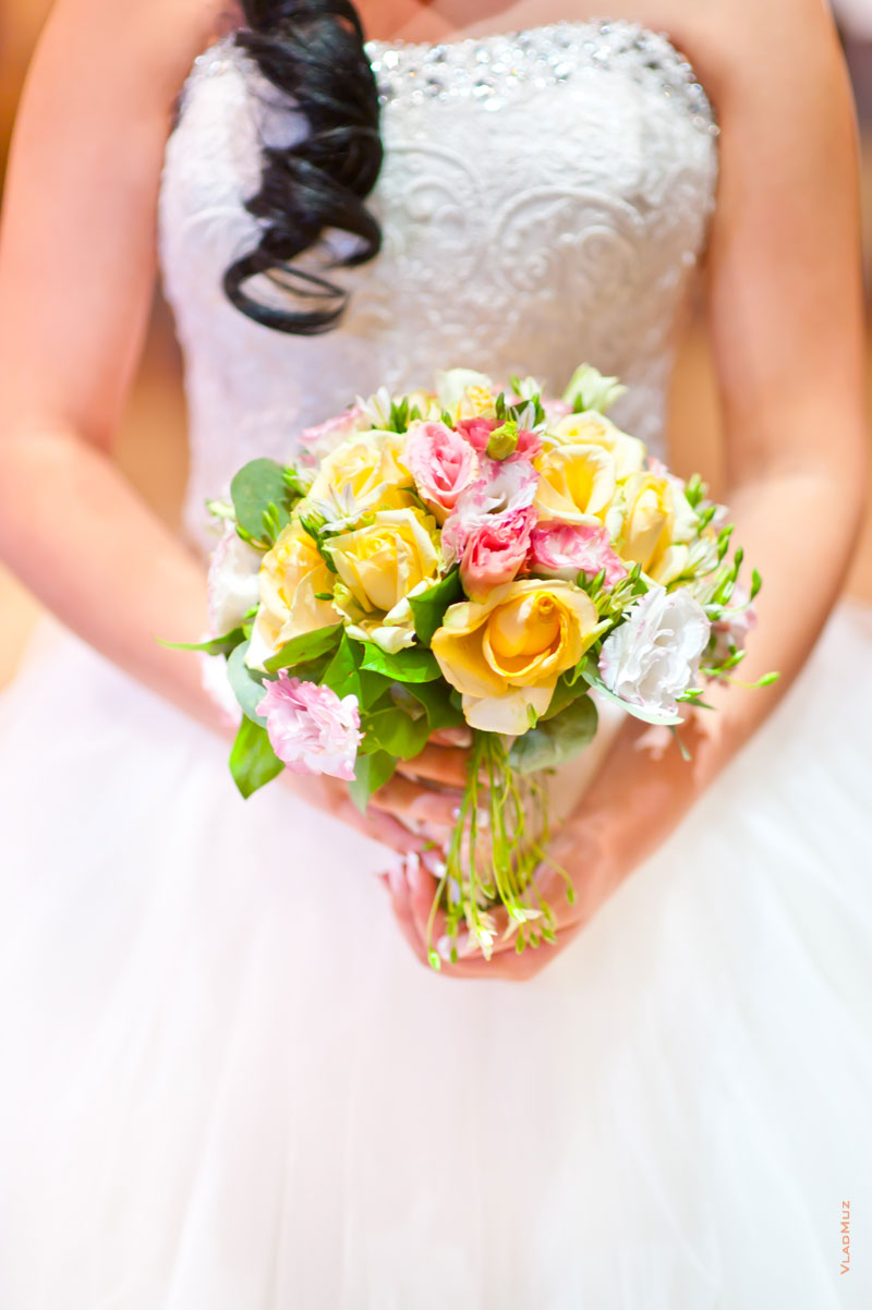 Фото свадебного букета в руках невесты на фоне белого свадебного платья