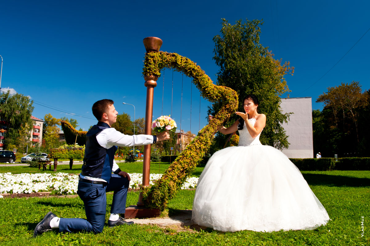 Фото жениха на колене с букетом и невесты у арфы, посылающей воздушные поцелуи