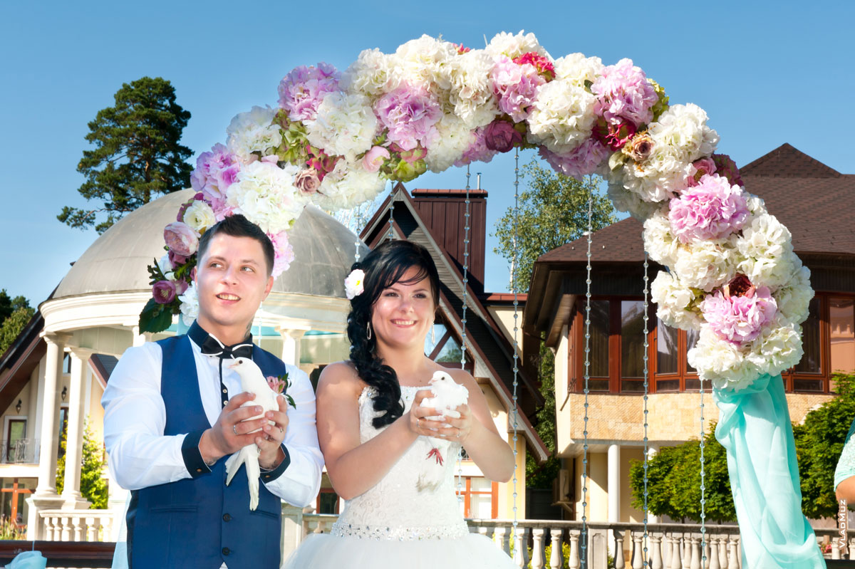 Фото жениха с невестой с белыми голубями на фоне свадебной арки
