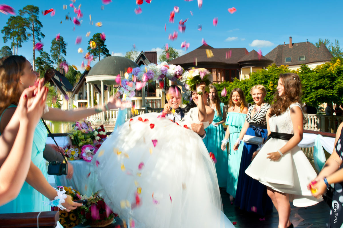 Фото жениха с невестой в руках под салютом из лепестков роз