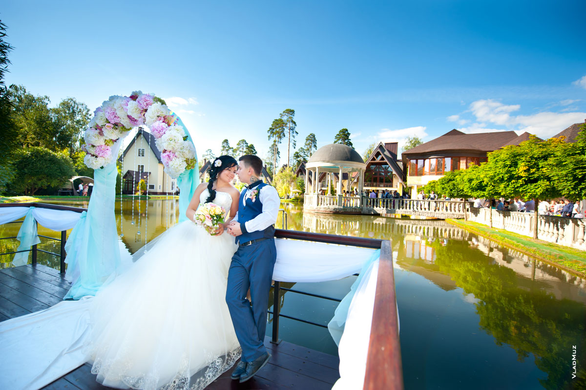 Фото жениха с невестой на берегу пруда, вдали ротонда и здания комплекса «Дворянское гнездо»