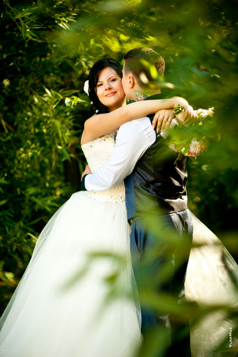 Фото свадебной пары в объятиях в парке на фоне зелени деревьев