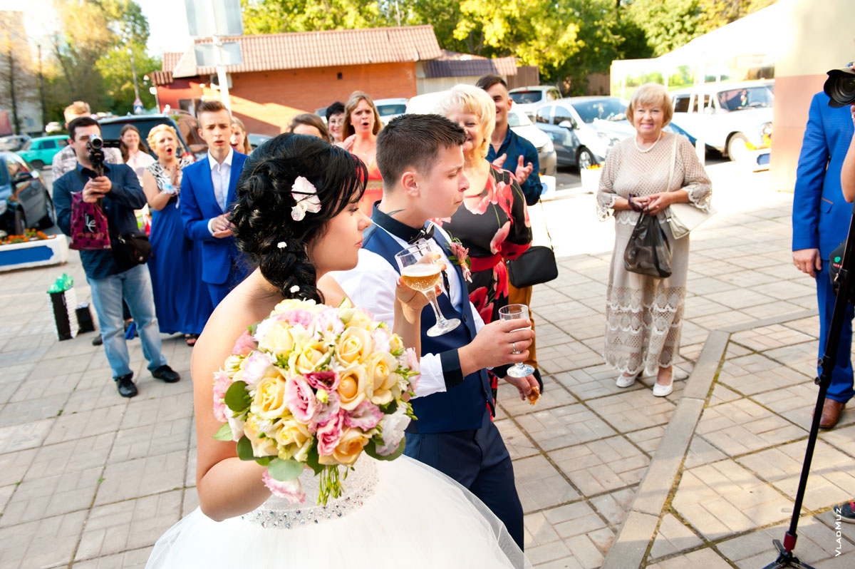 Фото жениха и невесты, пьющих перед входом в ресторан шампанское из бокалов