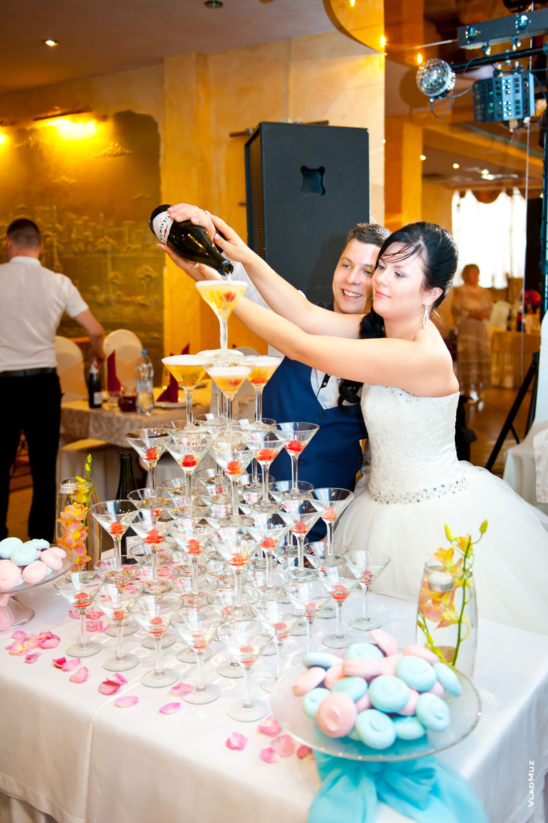 Фото жениха с невестой, наполняющих в ресторане шампанским пирамиду из бокалов