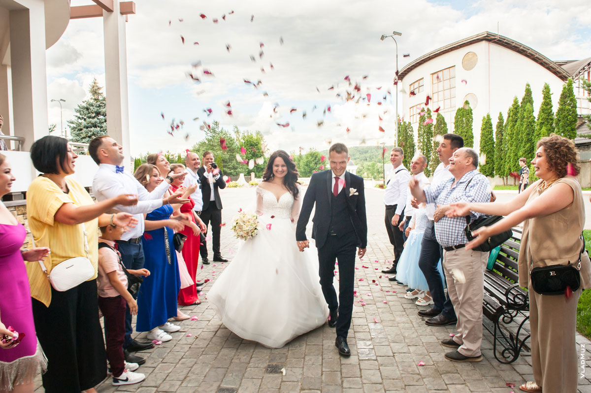 Фото идущих к караваю жениха и невесты, осыпаемых лепестками роз