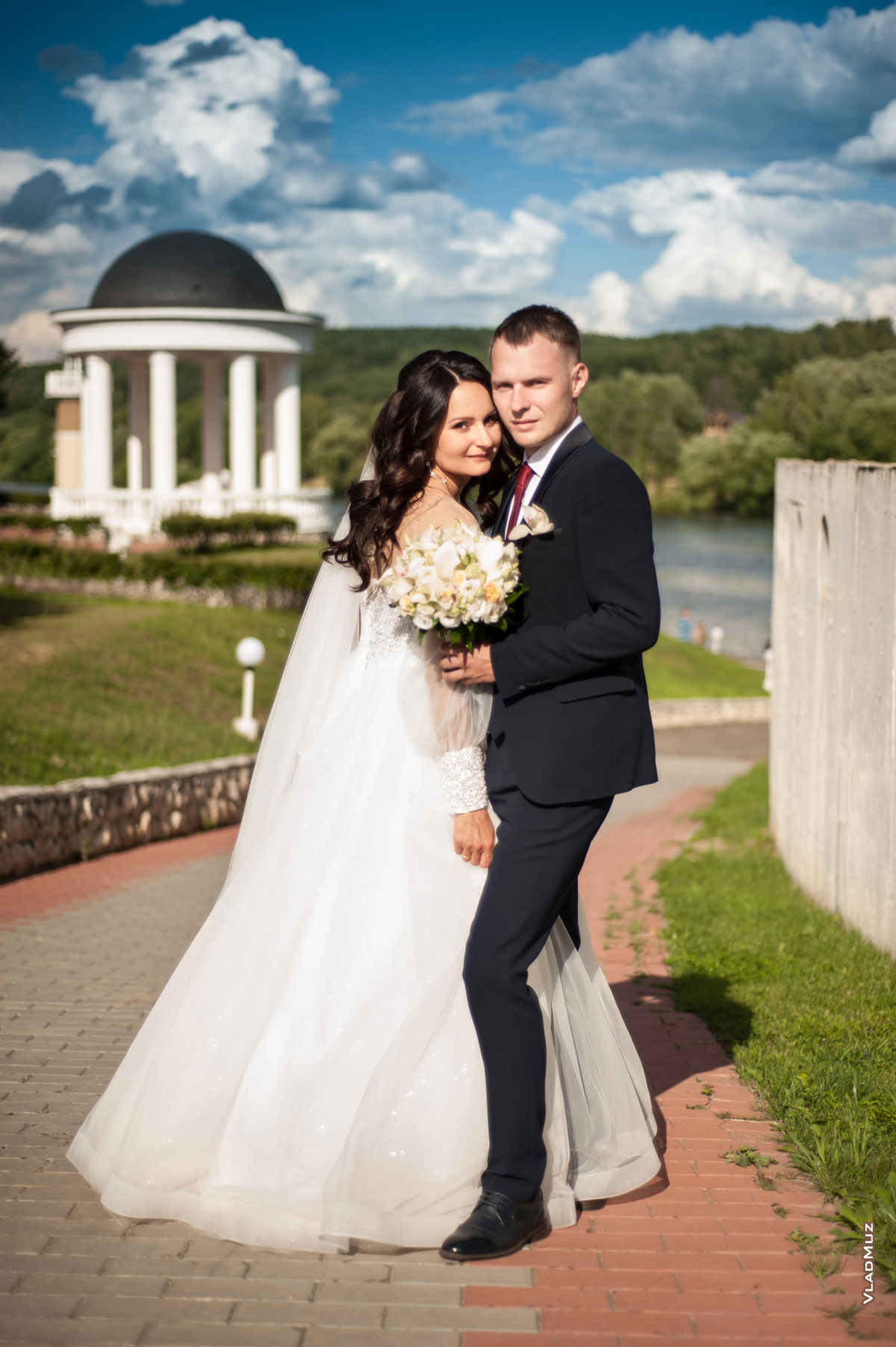 Фотопортрет свадебной пары в полный рост на фоне ротонды и синего облачного неба