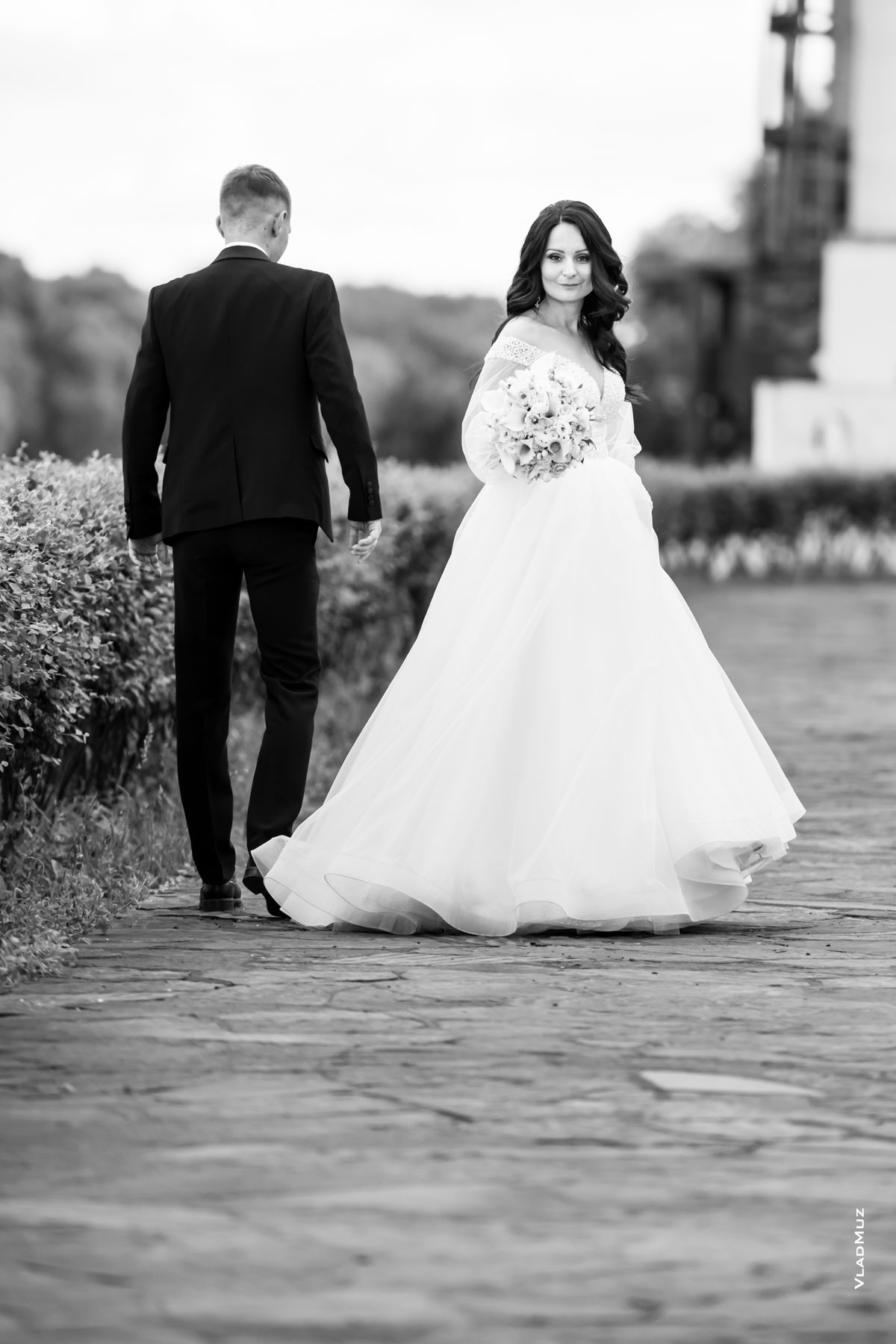 Ч/б фото во время свадебной прогулки: жених идет, невеста обернулась