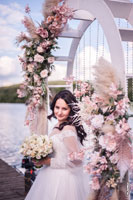 Поясной фотопортрет красивой невесты с букетом на фоне цветов свадебной арки