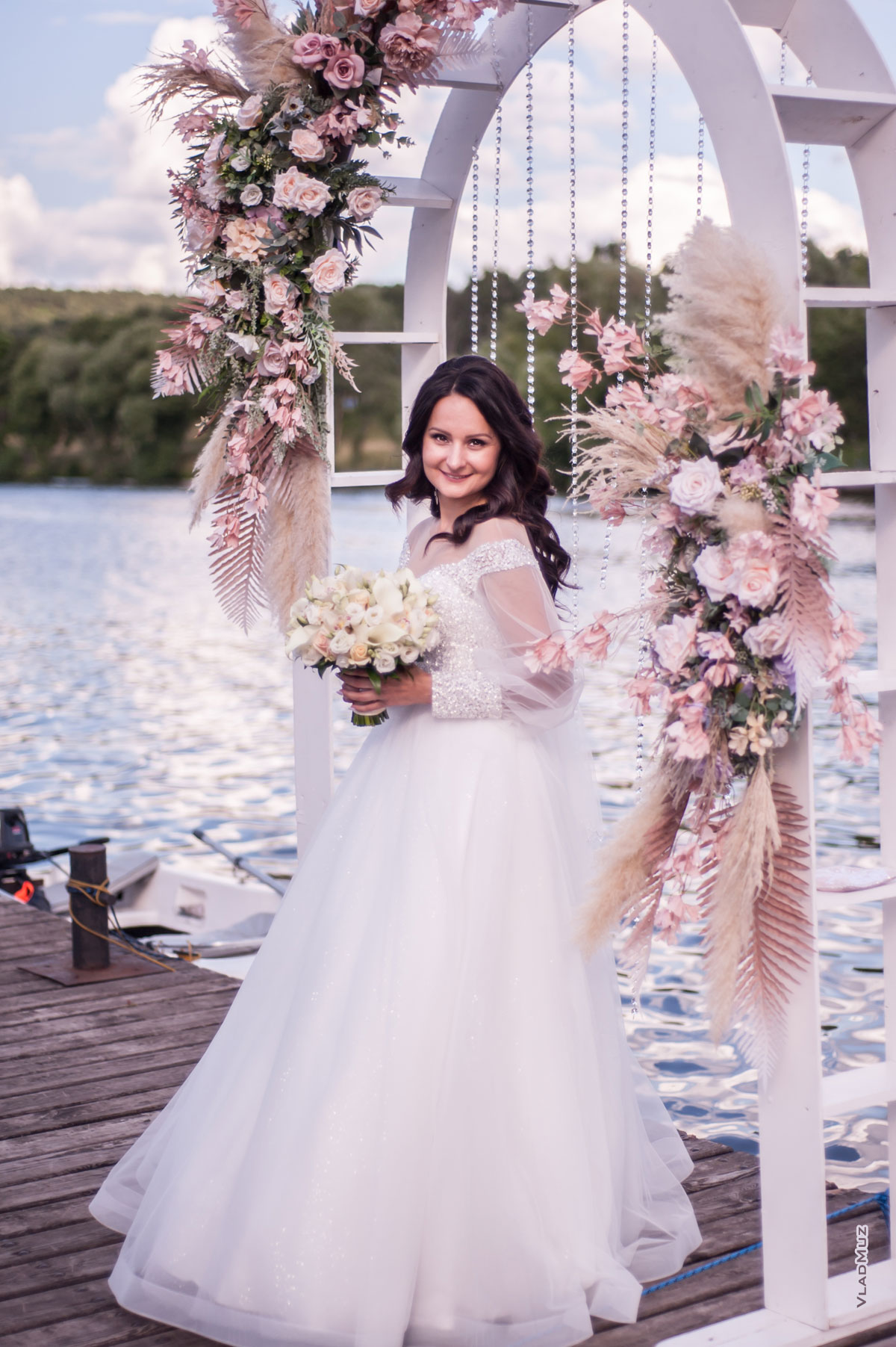 Фото красивой невесты в полный рост, с улыбкой, на фоне цветочной свадебной арки