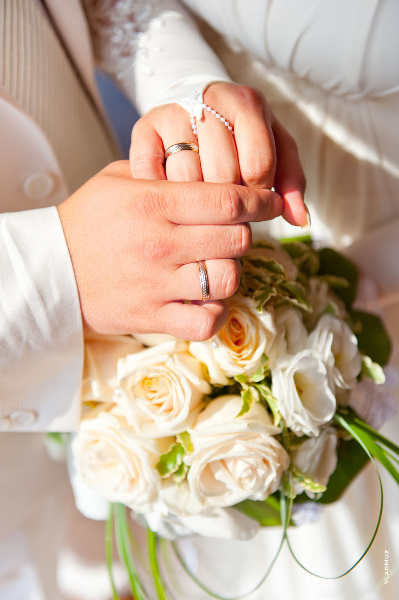 Светлая свадебная композиция: руки, кольца и белые цветы на белом фоне