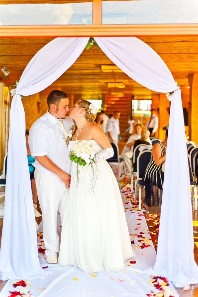 Фото 30 из галереи «Свадьба в «Малибу» - жених целует невесту в свадебной арке