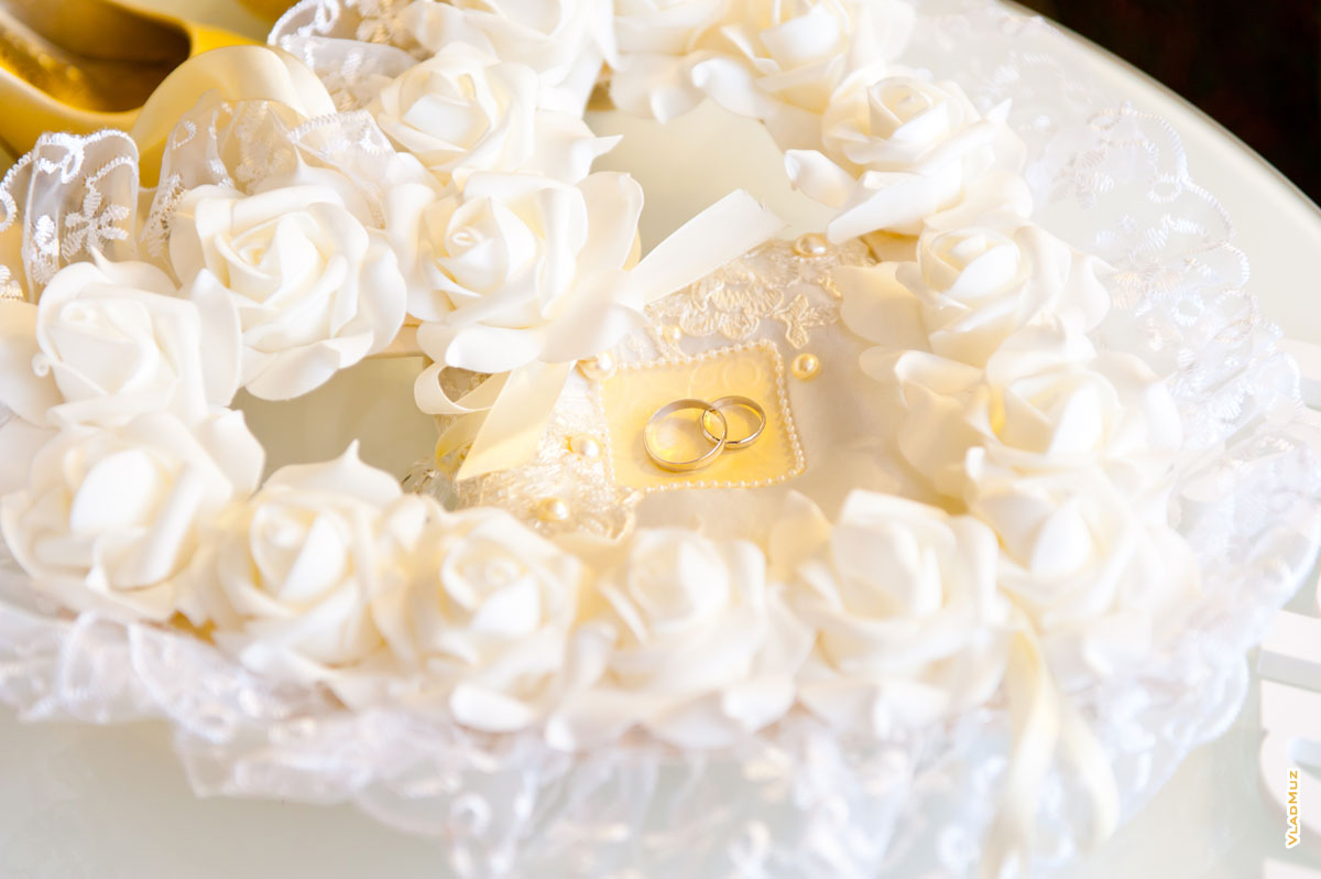 Фото свадебных колец на белой подушке в центре сердца из белых роз