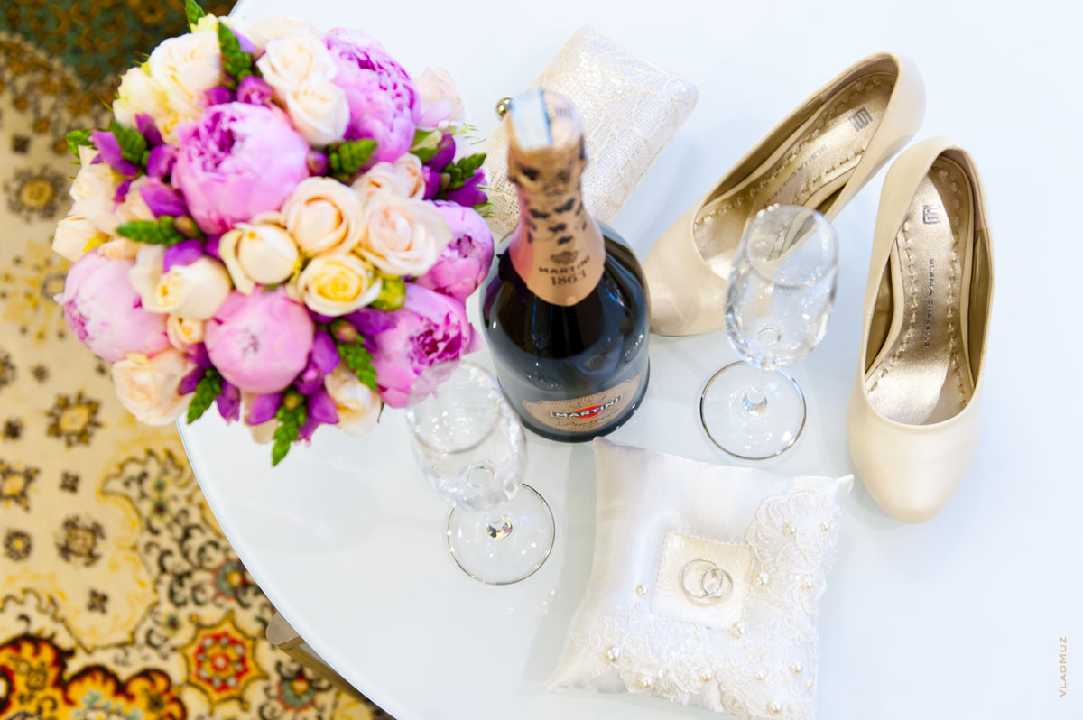 Свадебный фото натюрморт: вид сверху на букет невесты, бутылку шампанского с бокалами, свадебные кольца и туфли невесты