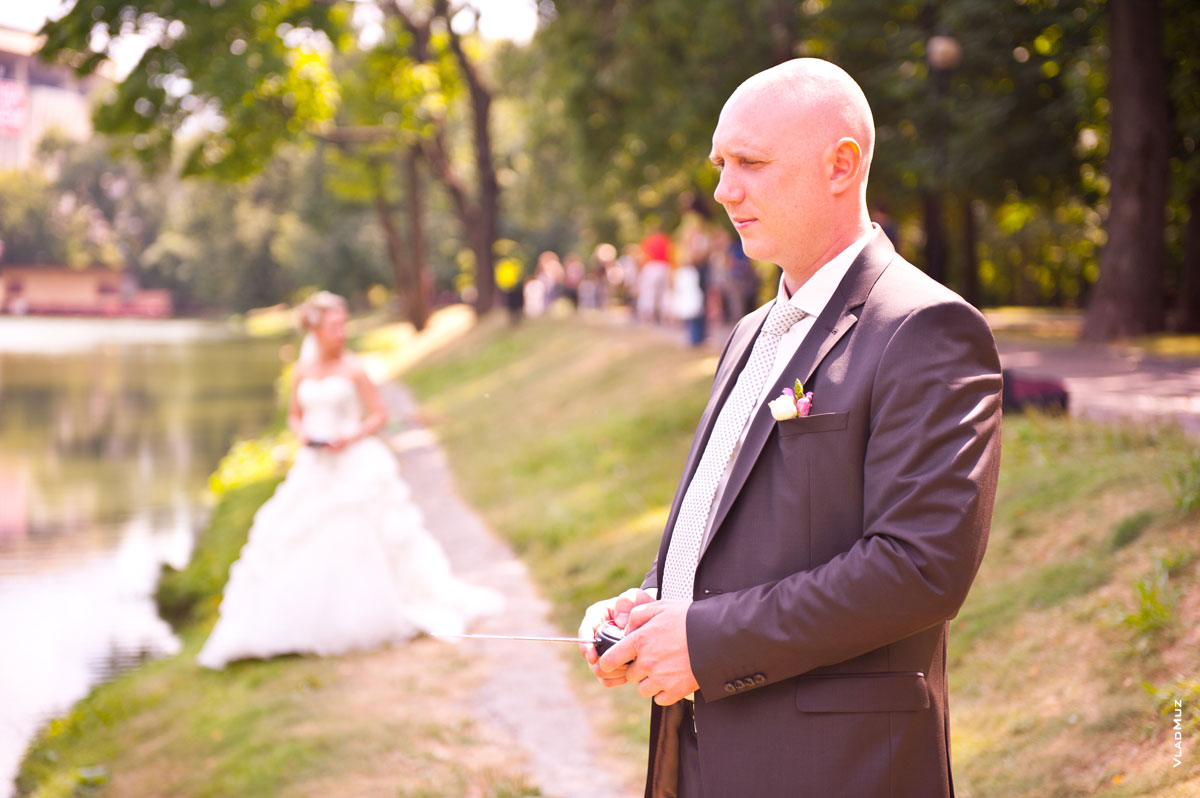 Фото жениха с пультом ДУ на переднем плане, вдали — невеста