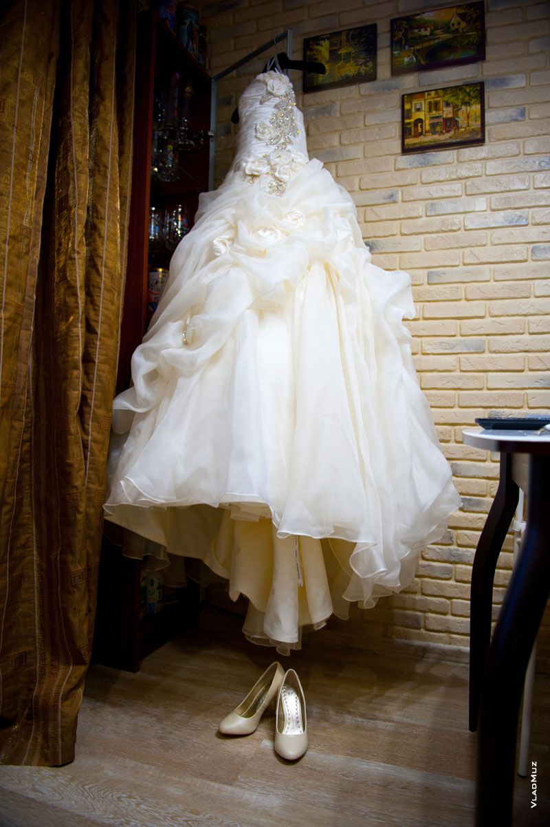 Фото свадебного платья на стене и туфель невесты на полу