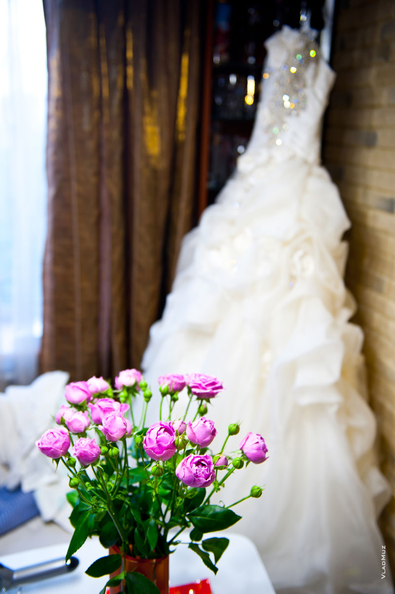 Фото роз на переднем плане, вдали — свадебное платье в расфокусе