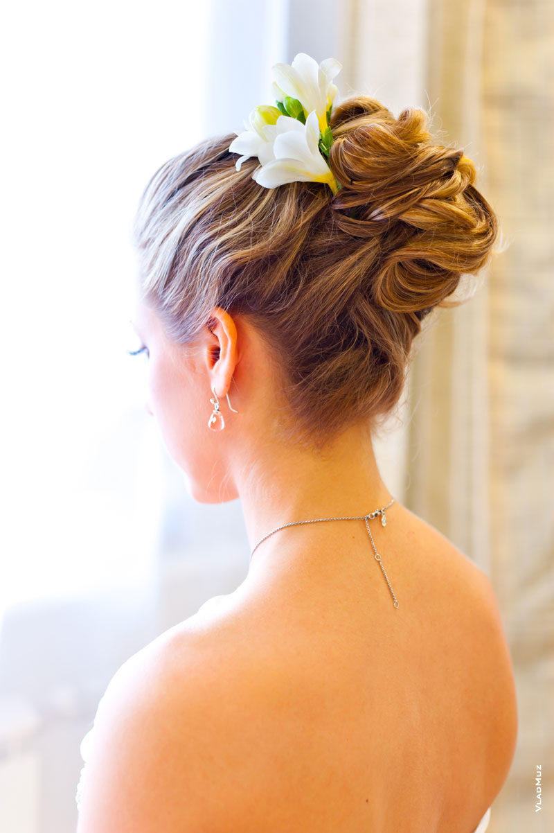 Фото прически невесты (вид сзади), в волосы вплетен живой цветок