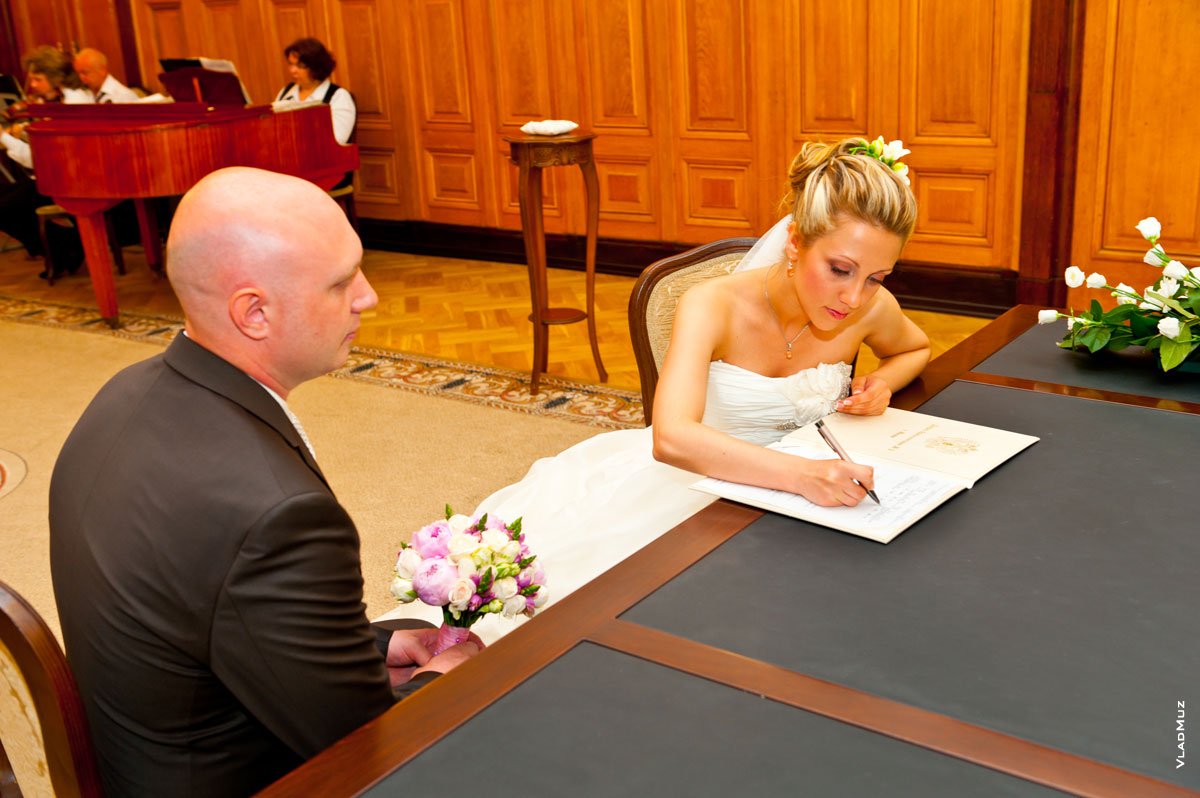 Фото невесты, ставящей подпись в свидетельстве о заключении брака