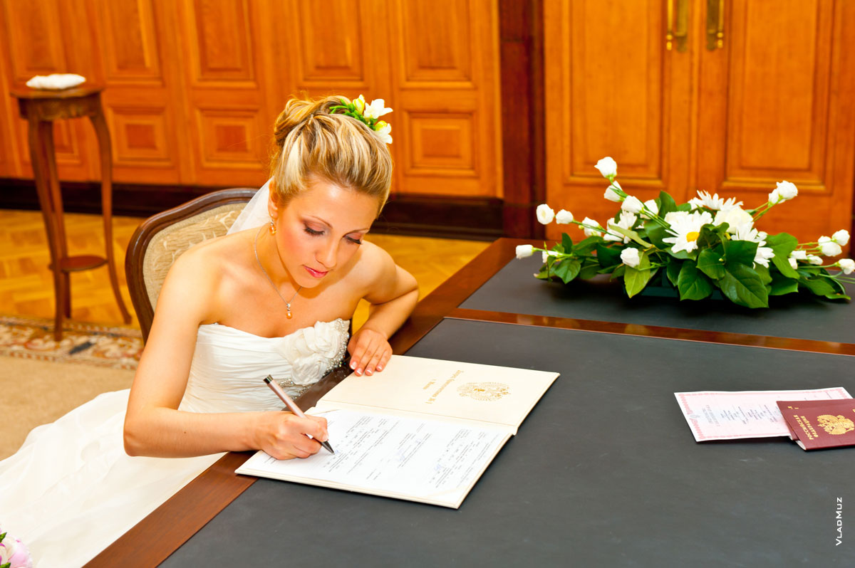 Фото невесты за столом в Грибоедовском ЗАГСе, ставящей подпись в свидетельстве