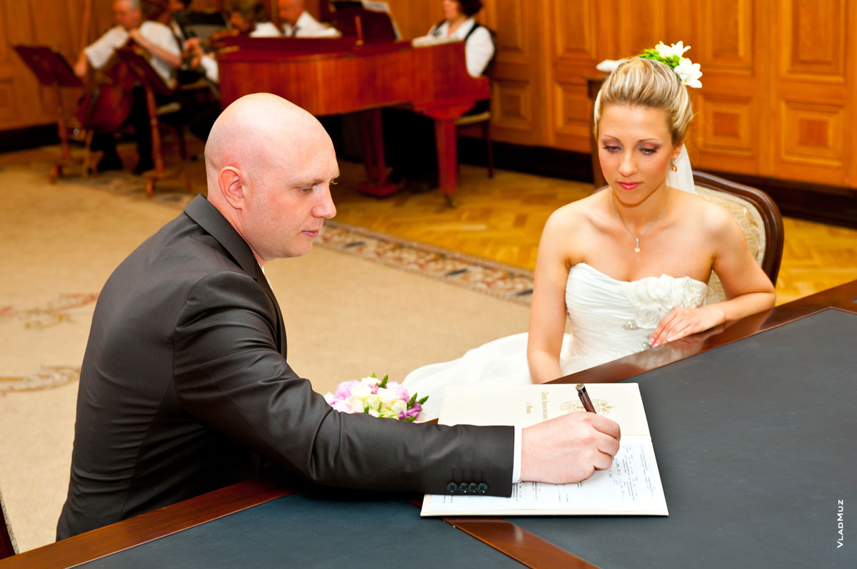 Фото жениха, сидя за столом, подписывающего документ о регистрации брака