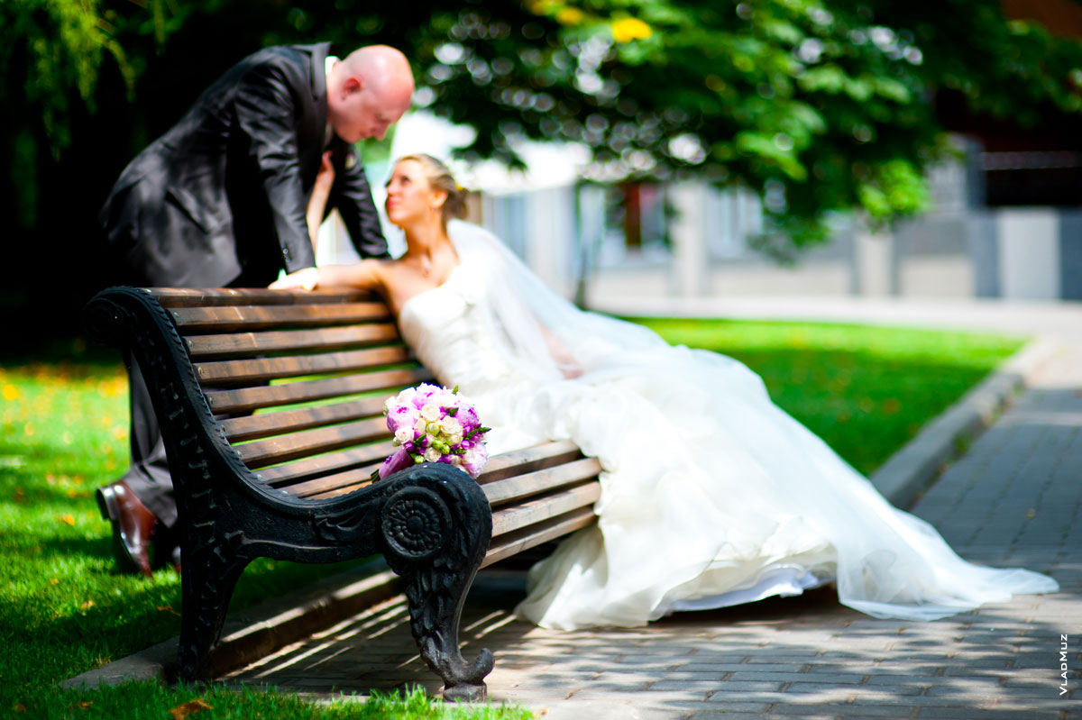 Фото букета невесты на лавочке в фокусе, жених и невеста вдали — в расфокусе
