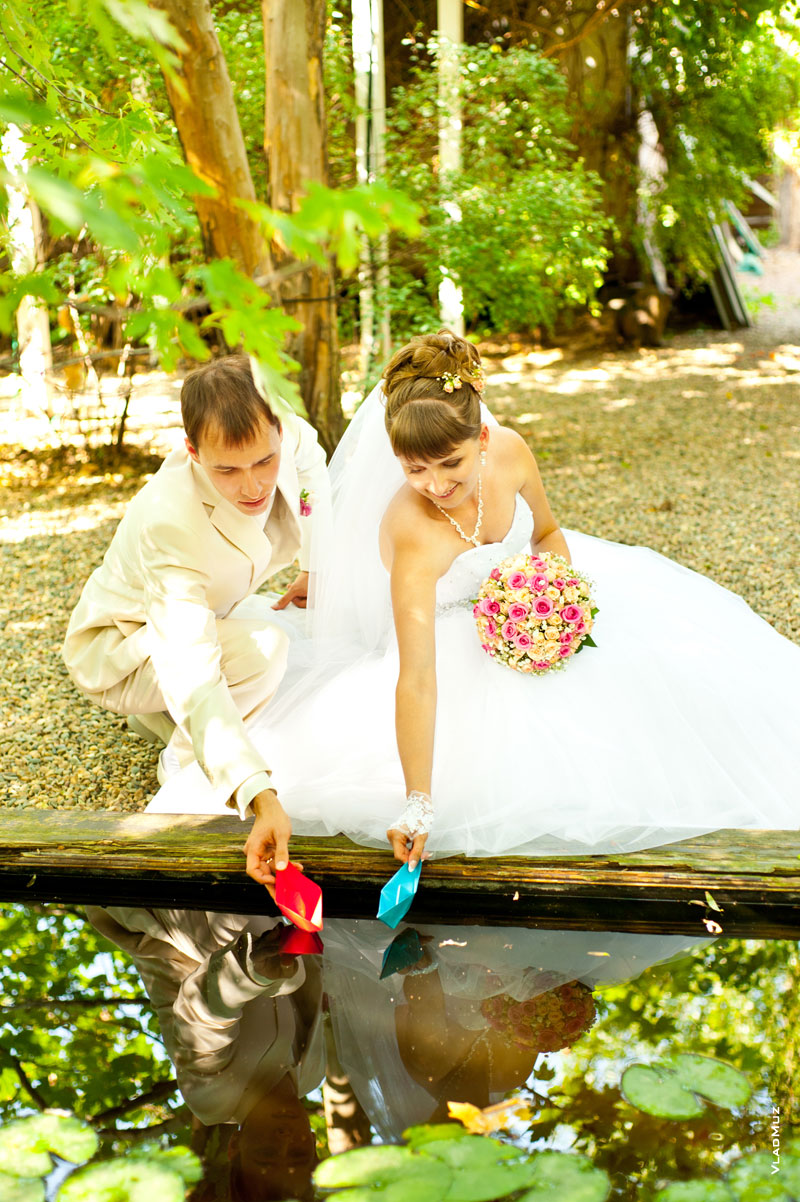 Фото свадебной пары, запускающей в пруду бумажные кораблики