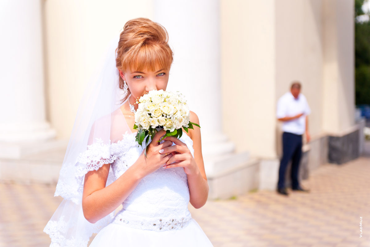 Фото невесты с букетом в фокусе и жениха вдали в расфокусе