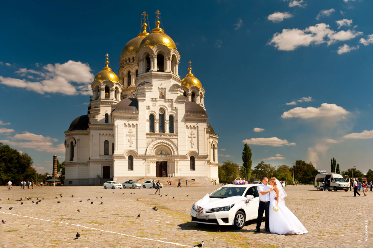 Фото свадебной пары рядом с автомобилем на фоне Вознесенского Войскового Кафедрального собора в Новочеркасске