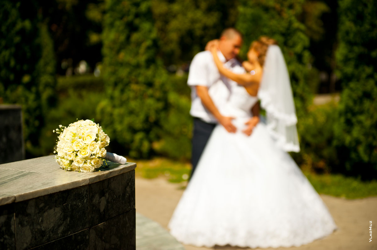 Фото букета невесты на переднем плане в фокусе, свадебной пары вдали в расфокусе