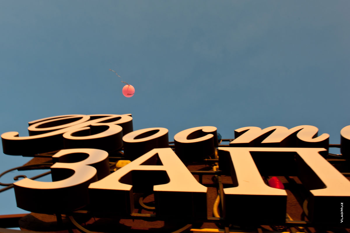 Фото улетающего в небо красного воздушного шара на фоне вывески кафе «Восток-Запад»