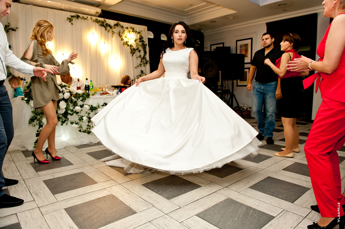 Фото танцующей невесты со шлейфом свадебного платья среди гостей в кафе