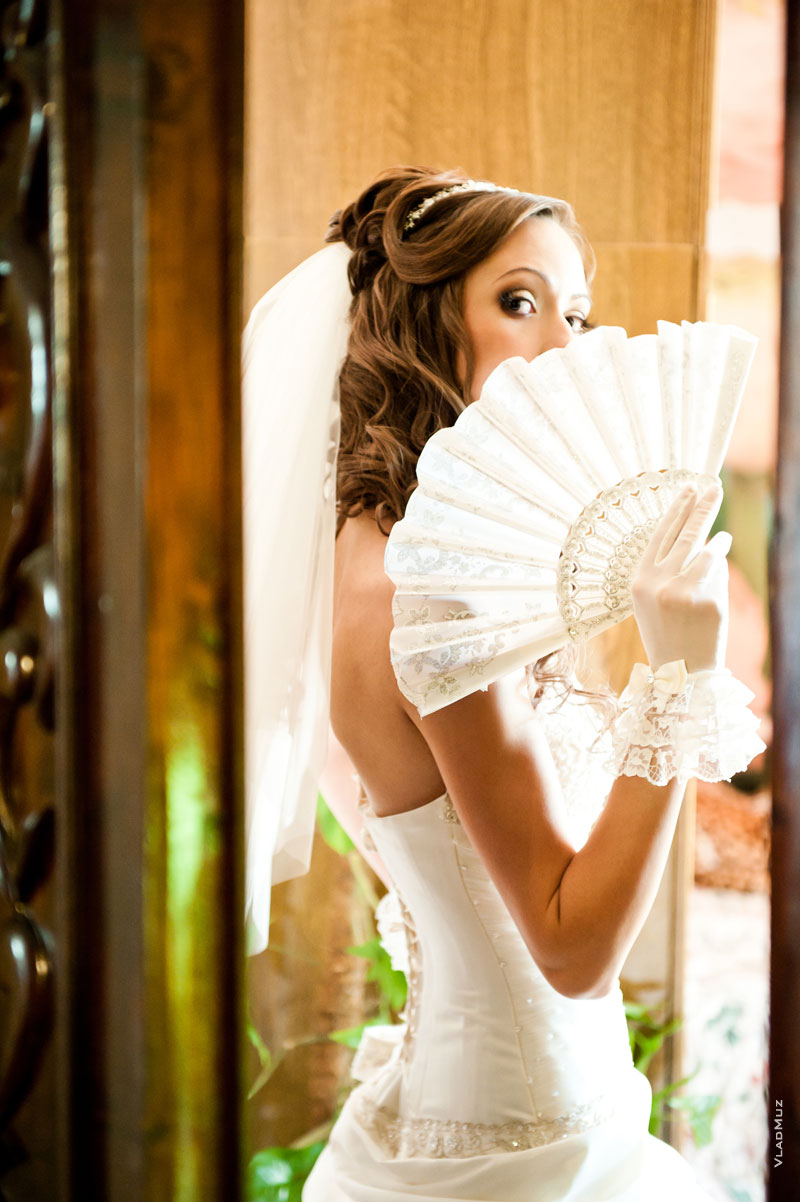 Свадебный фотопортрет невесты с веером сделан через дверной проем, как подглядывание за моделью