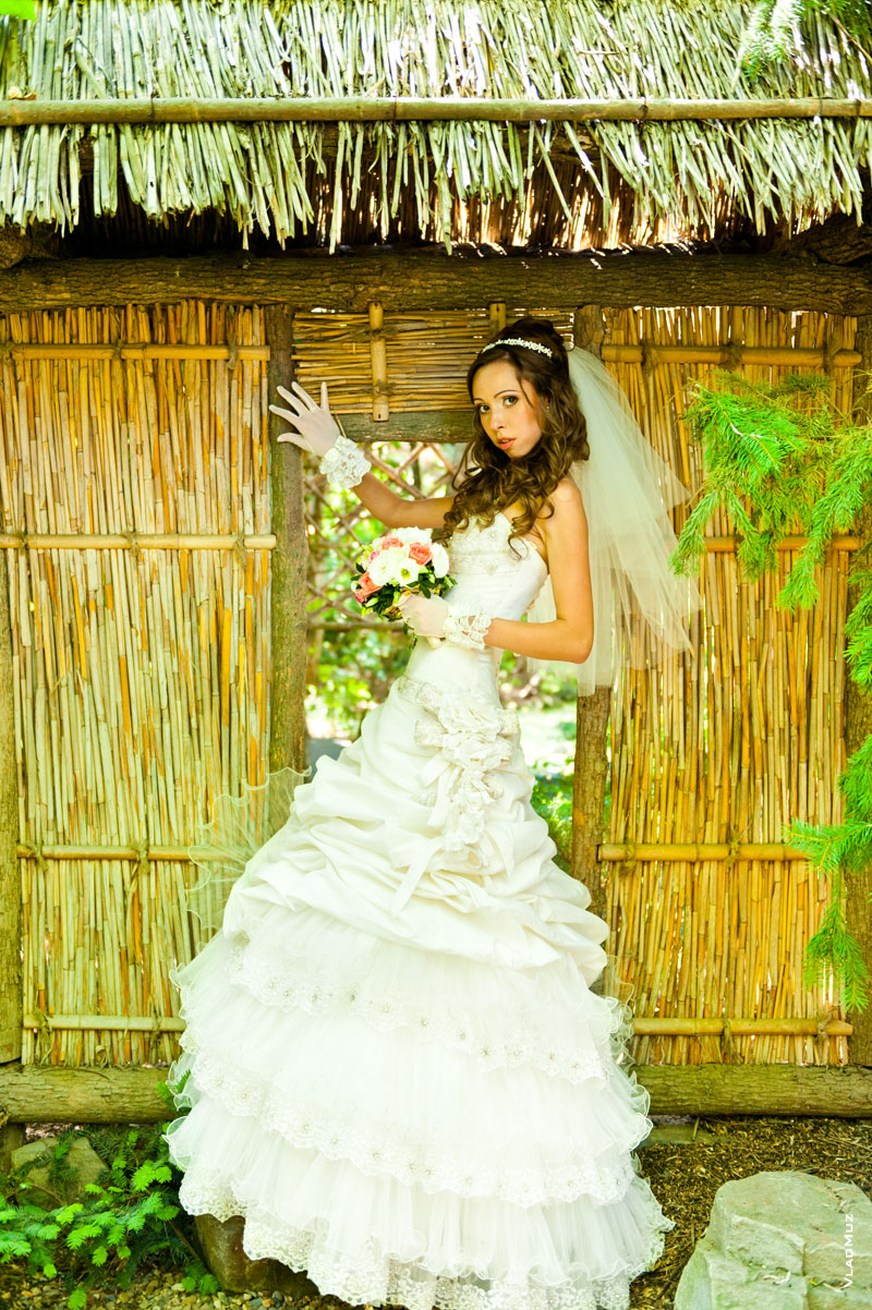Фото невесты в саду Толоконникова у плетенной стены из камыша